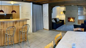 Une cuisine moderne avec des meubles en bois et un coin bar, une table à manger avec des chaises, et une cheminée dans l’espace salon.