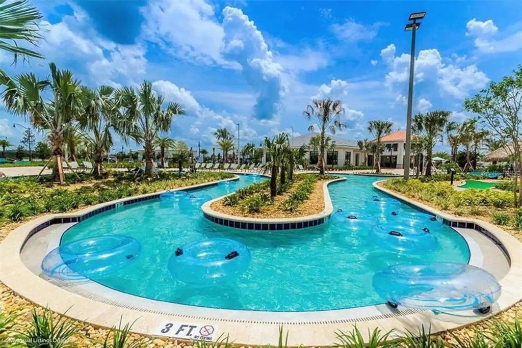 Una piscina con varias pistas, rodeada de palmeras y un edificio al fondo.