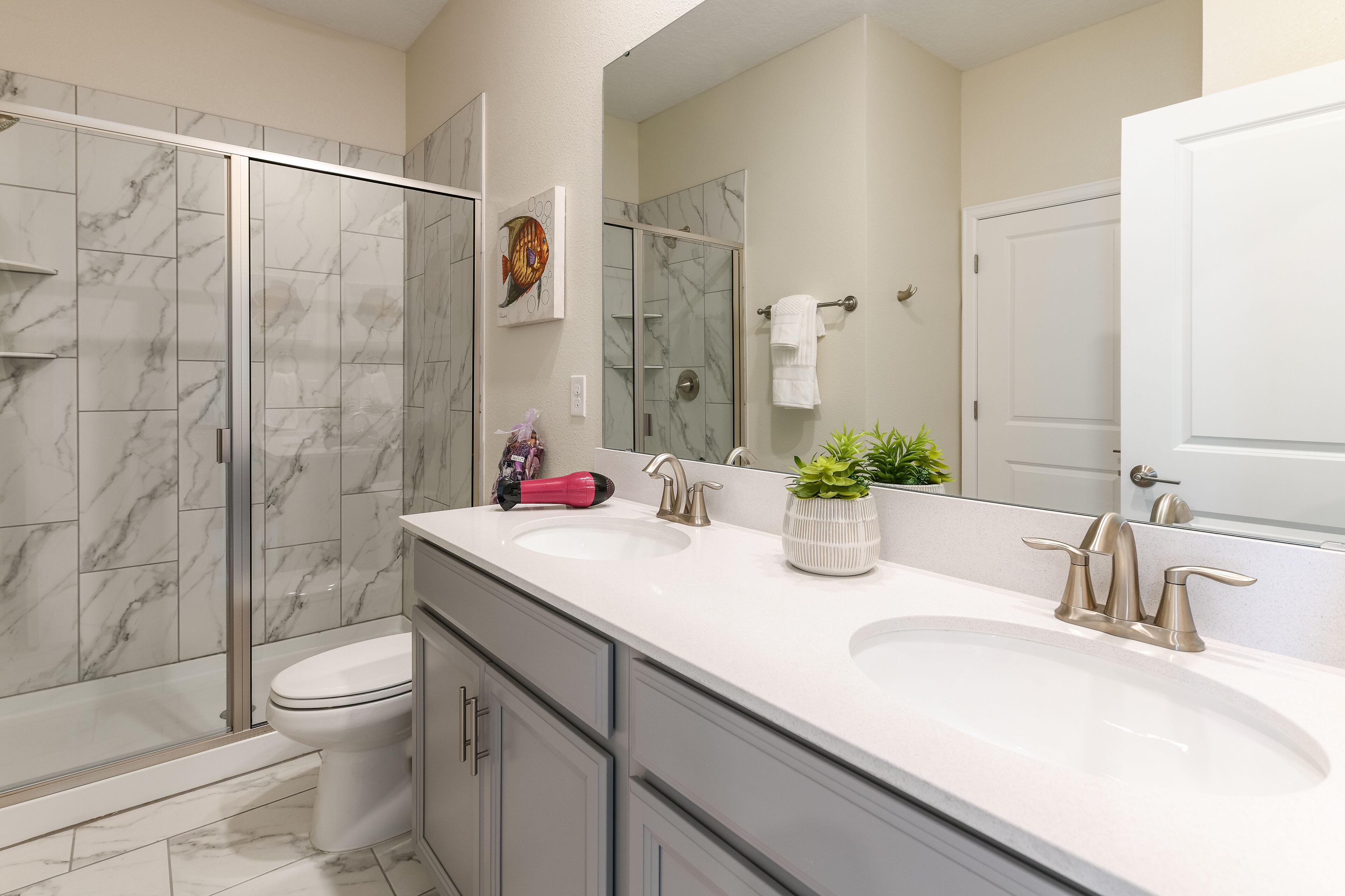 A modern bathroom with two sinks, a glass shower enclosure, and a toilet.