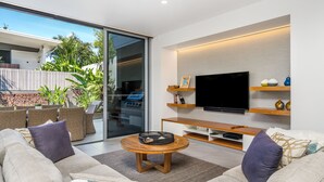 A modern living room with a large flat-screen TV, comfortable seating, and a glass door leading to an outdoor area. - Kokos Beach House 4 (Byron Bay)