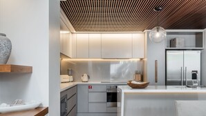 A modern kitchen with a central island, built-in appliances, and a wooden ceiling. - Kokos Beach House 4 (Byron Bay)