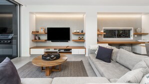 A modern living room with a flat-screen TV, wooden shelves, a sofa, and a coffee table. - Kokos Beach House 4 (Byron Bay)