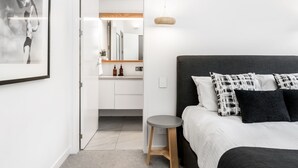 A modern bedroom with a bed, a bedside table, a hanging light, and a bathroom visible through an open door. - Kokos Beach House 4 (Byron Bay)