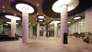 Een ruime lobby met een modern design, met grote ronde plafondlampen, een centrale trap en een goed zicht op de ingang van een gebouw.