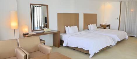 A hotel room with a large bed, a desk, a chair, a mirror, and a bedside table with a lamp.