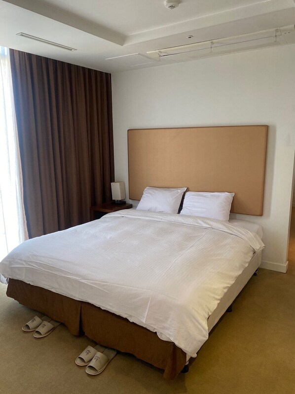 Une chambre d’hôtel avec un grand lit, une table de chevet, une lampe et une vue sur l’extérieur à travers les rideaux.