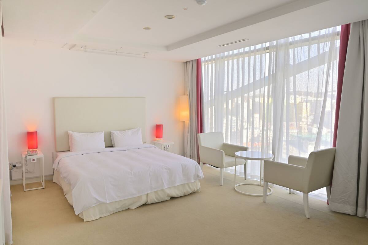A hotel room with a large bed, two bedside lamps, a small table, and a chair.