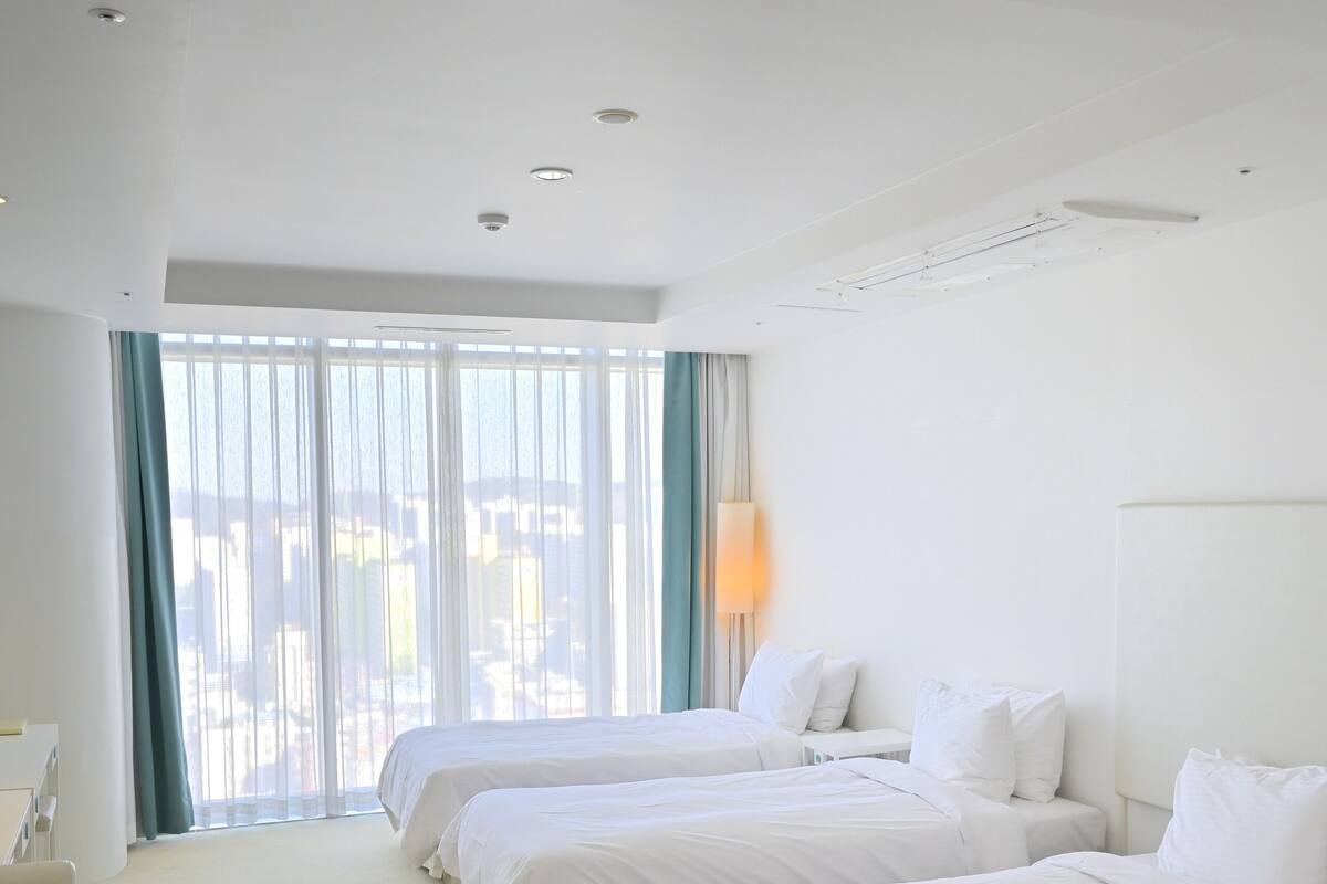 A hotel room with two beds, a desk, and a large window with curtains.