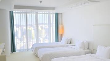 A hotel room with two beds, a desk, and a large window with curtains.