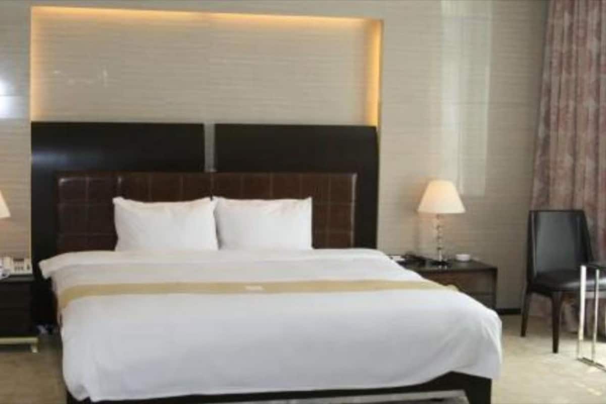A hotel room with a large bed, two bedside tables with lamps, a headboard, and a chair.