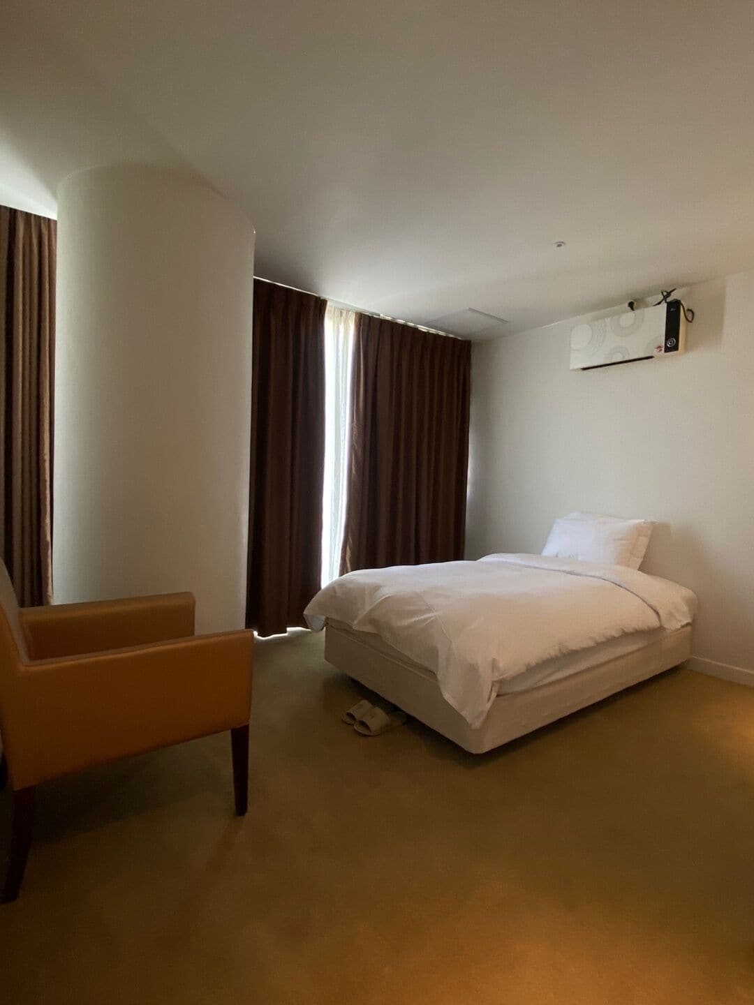 A hotel room with a bed, a chair, and an air conditioning unit on the wall.