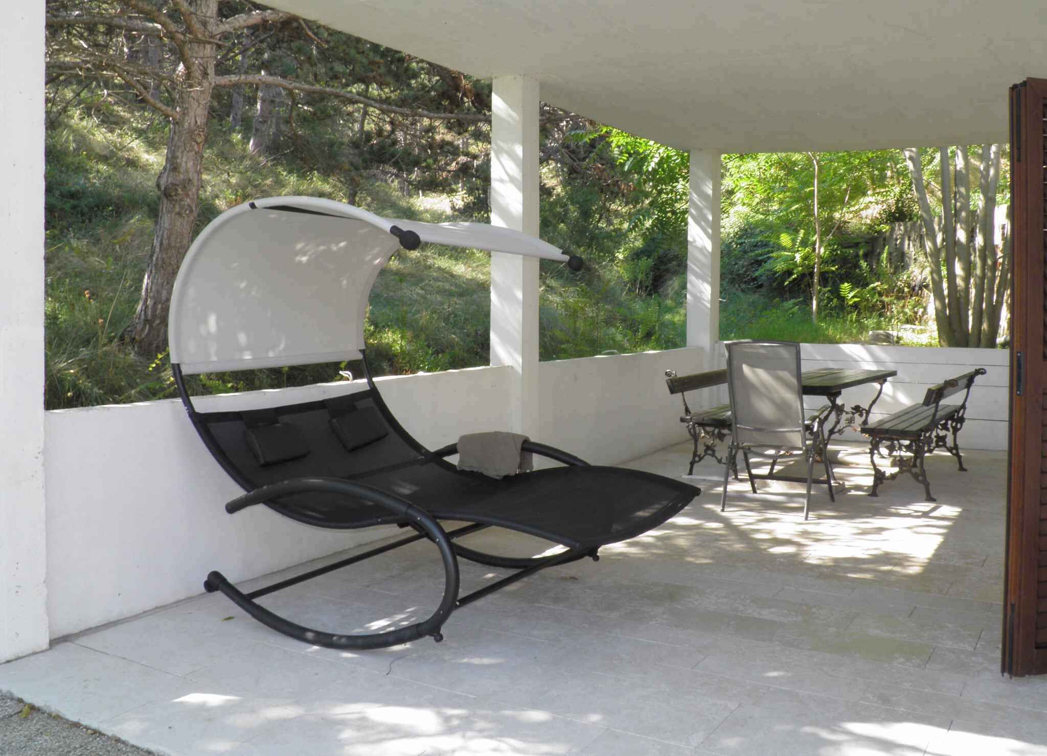 Un espace extérieur abrité avec un coin salon comprenant un fauteuil et une table avec des chaises.
