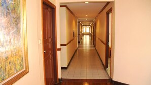 A long, narrow hotel corridor with wooden doors and tiled flooring. - Shagwell Mansions Pattaya (Pattaya)