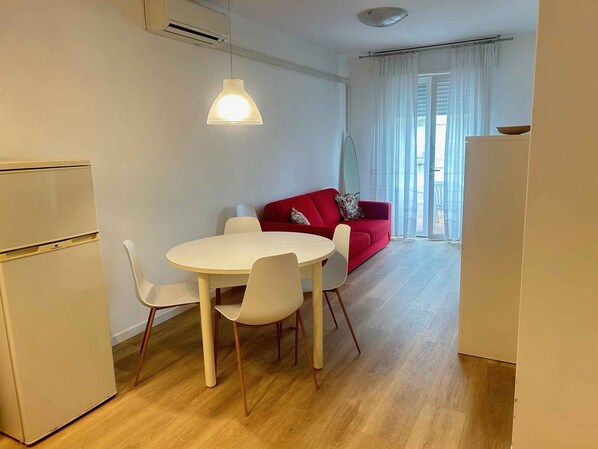 A compact living space with a dining area, a red sofa, and a view through a window.