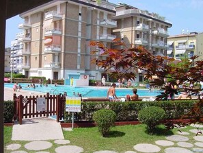A multi-story residential building with balconies, a swimming pool, and a gated entrance.