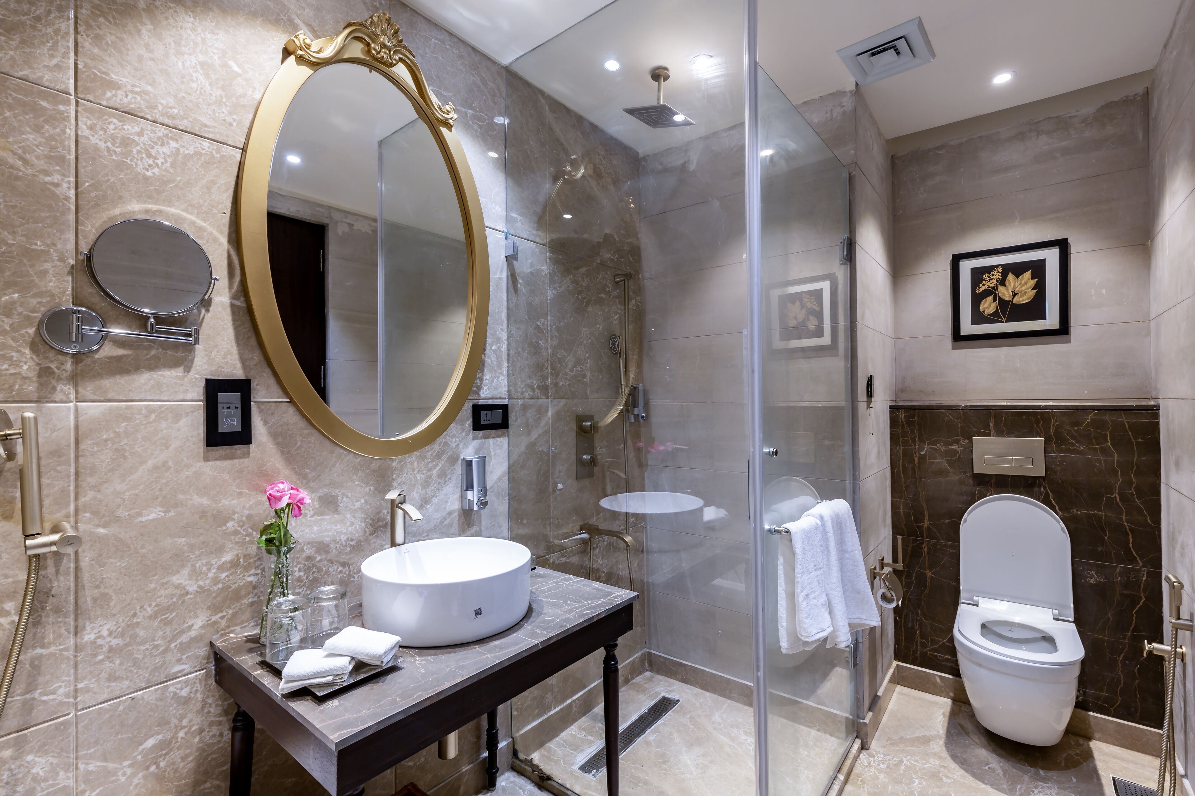 A modern bathroom with a round mirror, a round sink, a toilet, and a glass-enclosed shower.