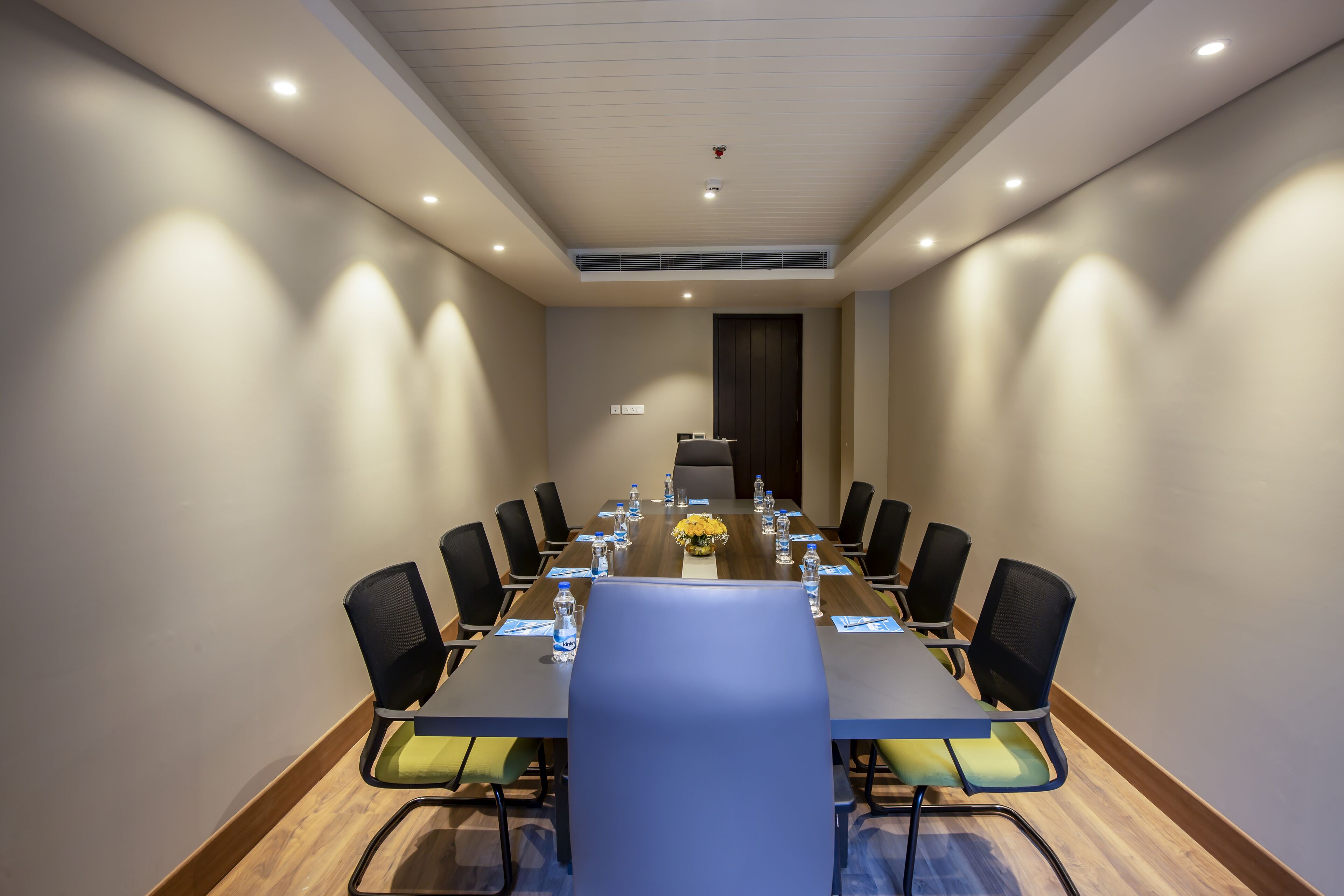 Un salón de conferencias con una larga mesa, sillas y una pantalla pequeña.