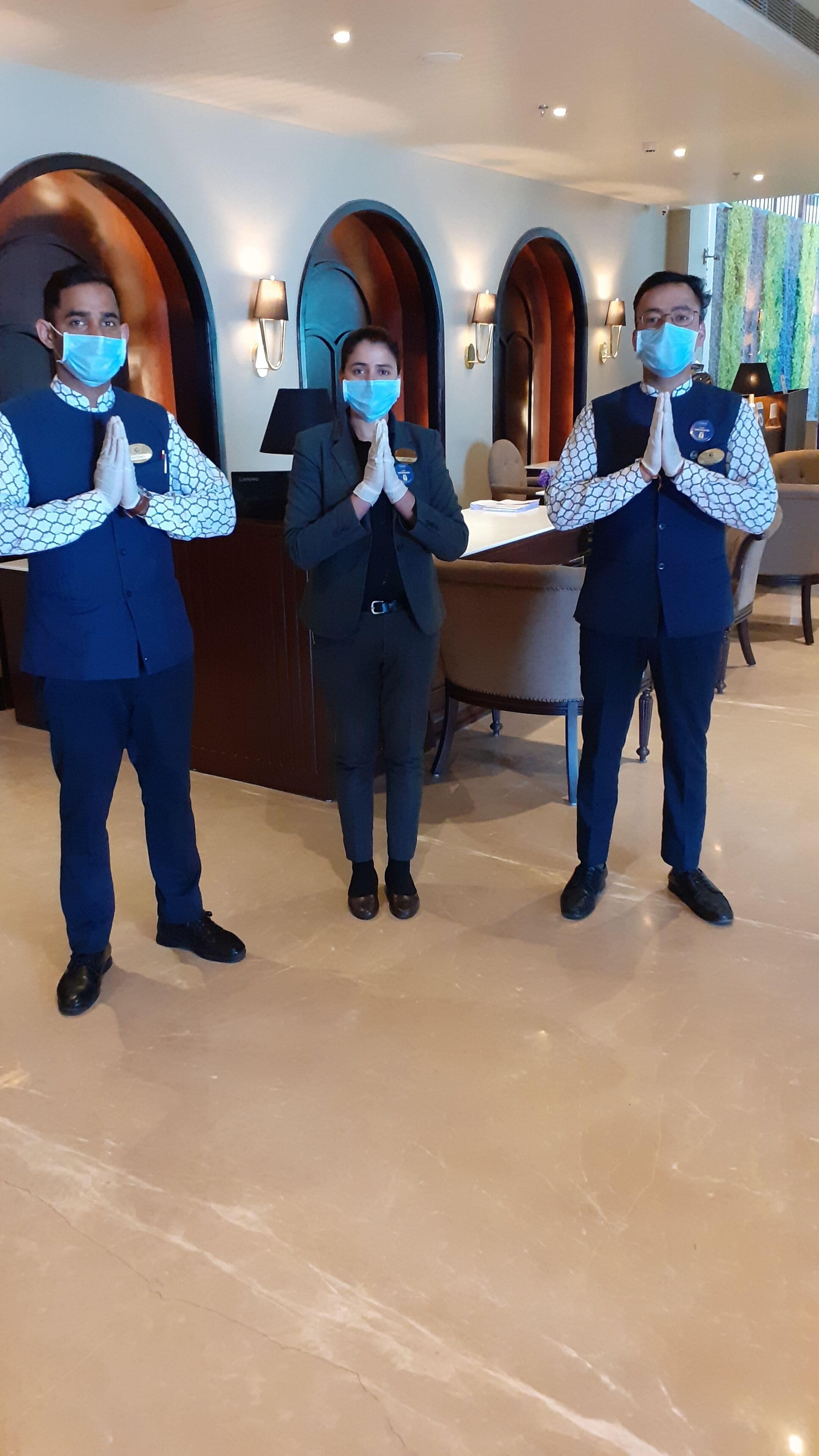 Three staff members in uniform standing in a lobby with a marble floor and a reception desk.