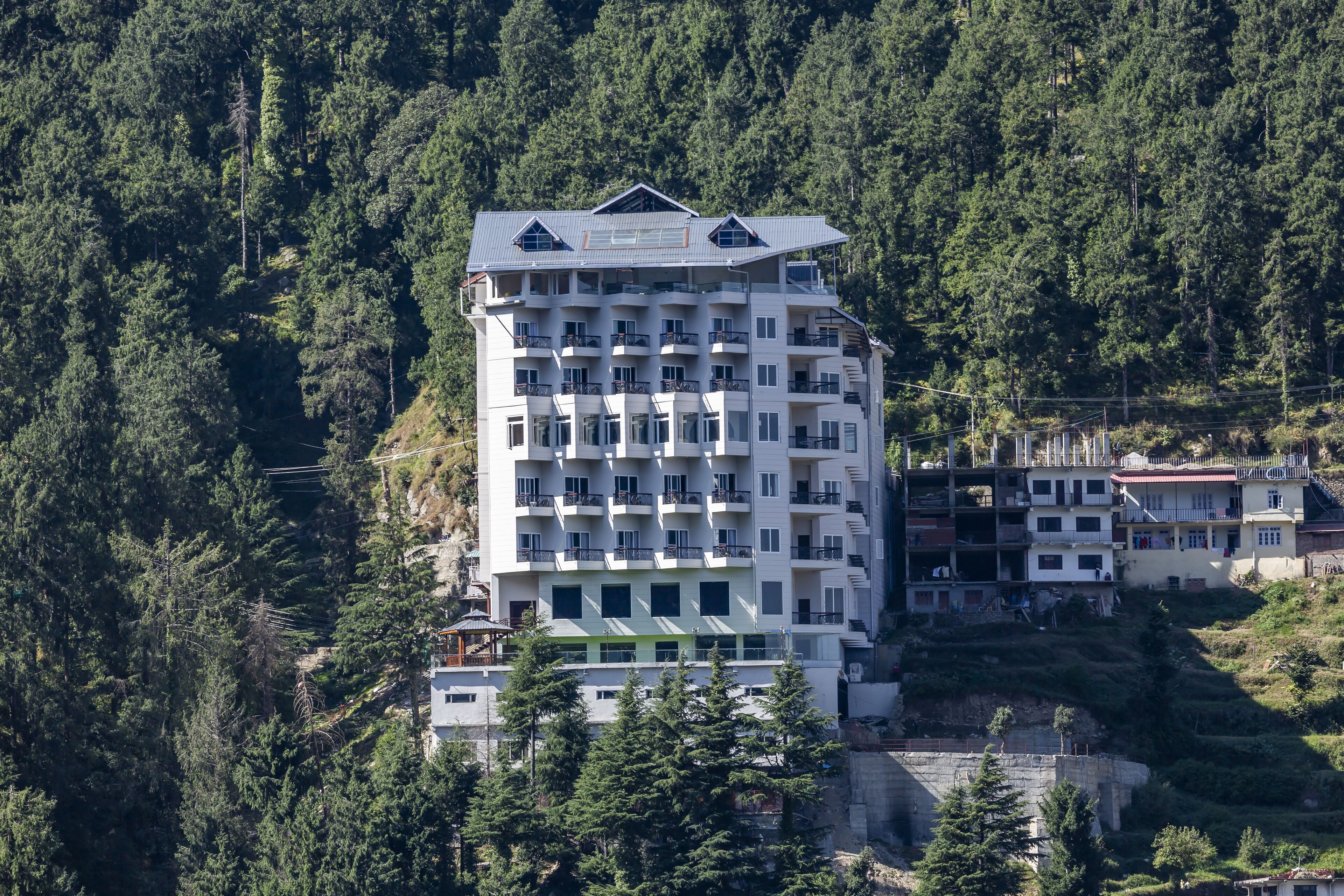 Un hôtel à plusieurs étages, doté de balcons et entouré d’une forêt dense.