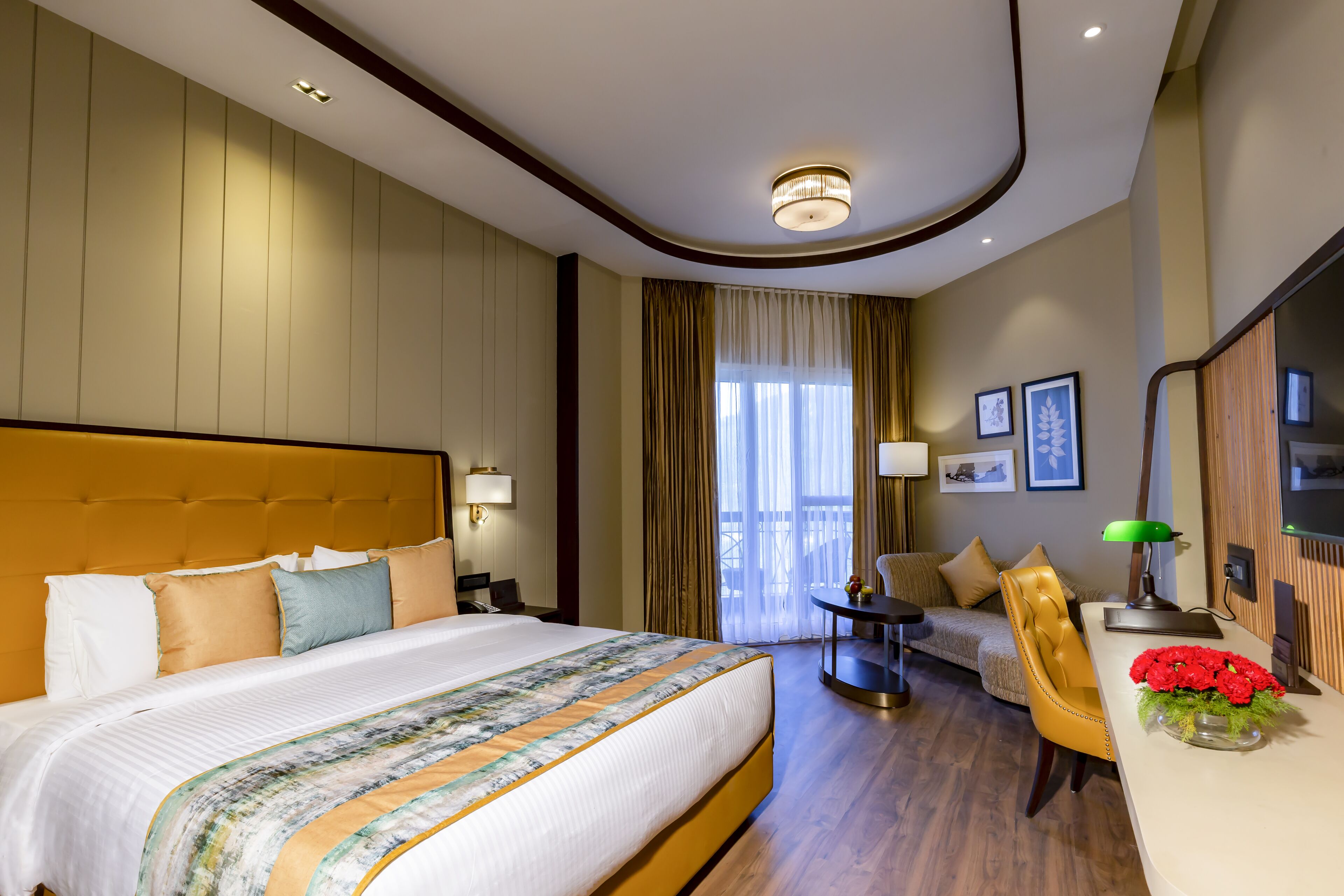 A hotel room with a large bed, a desk with a lamp, a chair, and a sofa.