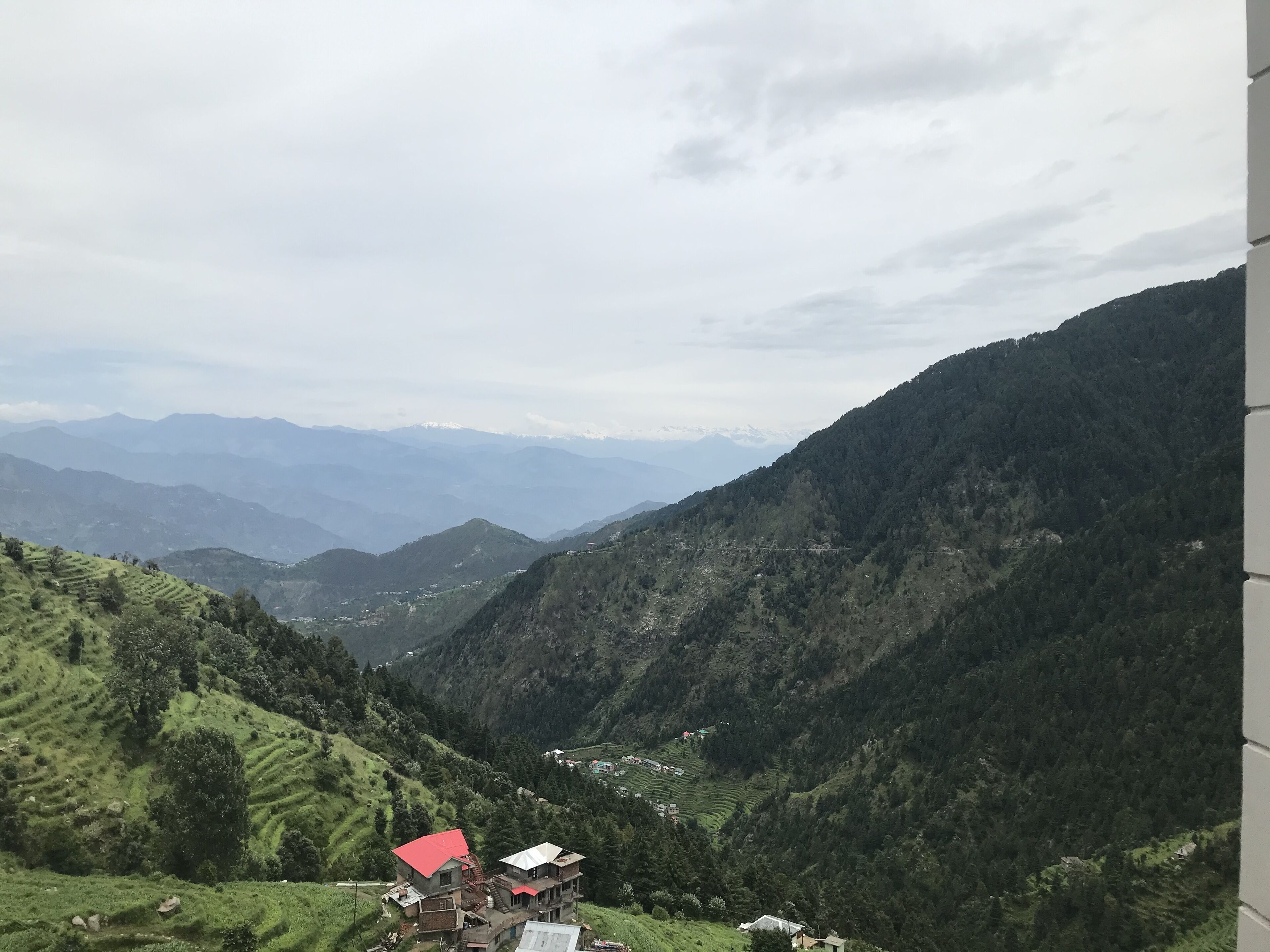 Paisaje montañoso con campos en terrazas y algunos edificios de techos rojos y blancos.