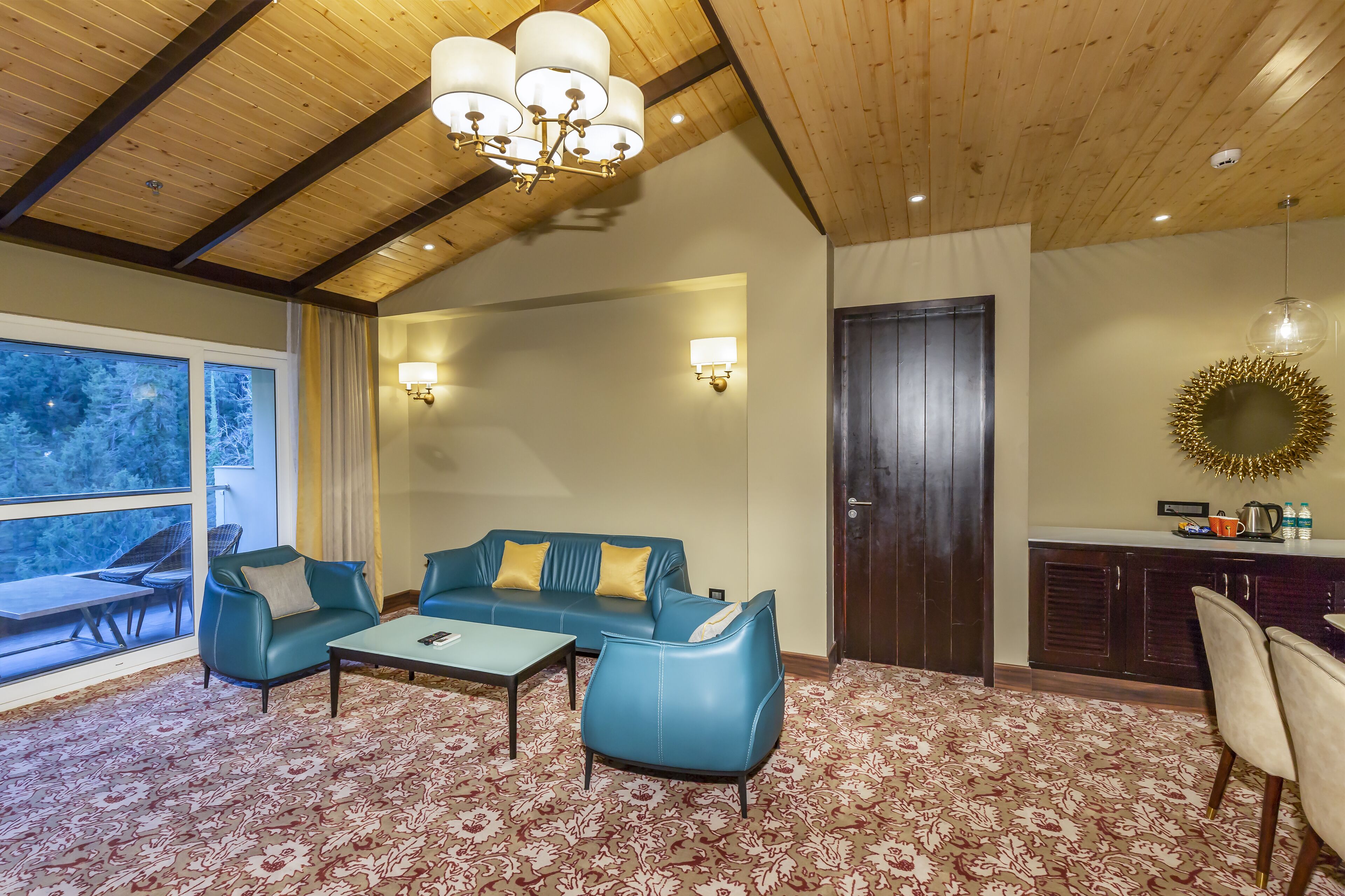Quarto com teto de madeira, sofá azul e um tapete estampado, além de um espaço de jantar com cadeiras.