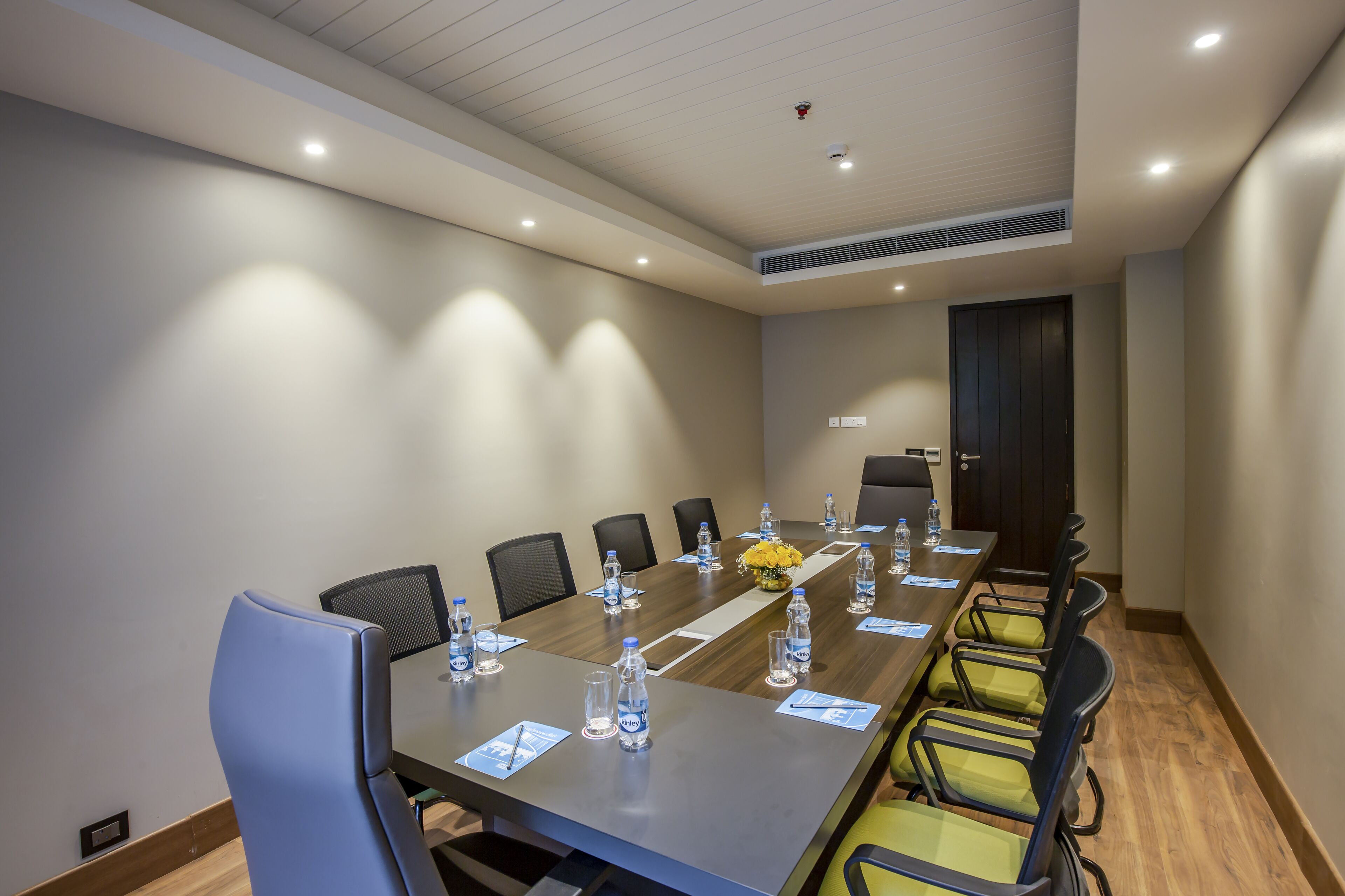 Un salón de conferencias con una mesa larga, sillas, botellas de agua y un florero.