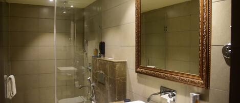 Un baño moderno con cabina de ducha de vidrio, tocador de mármol y un espejo grande con marco decorativo.