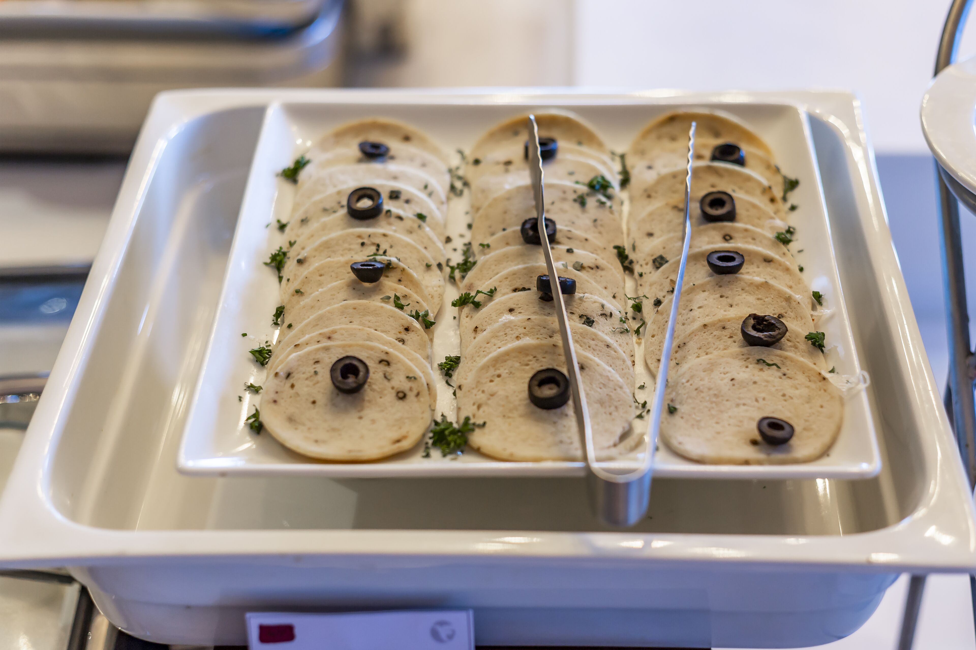 Bandeja de tortillas rebanadas con aceitunas negras y hierbas, probablemente para un servicio de buffet o catering.