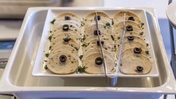 Bandeja de tortillas rebanadas con aceitunas negras y hierbas, probablemente para un servicio de buffet o catering.