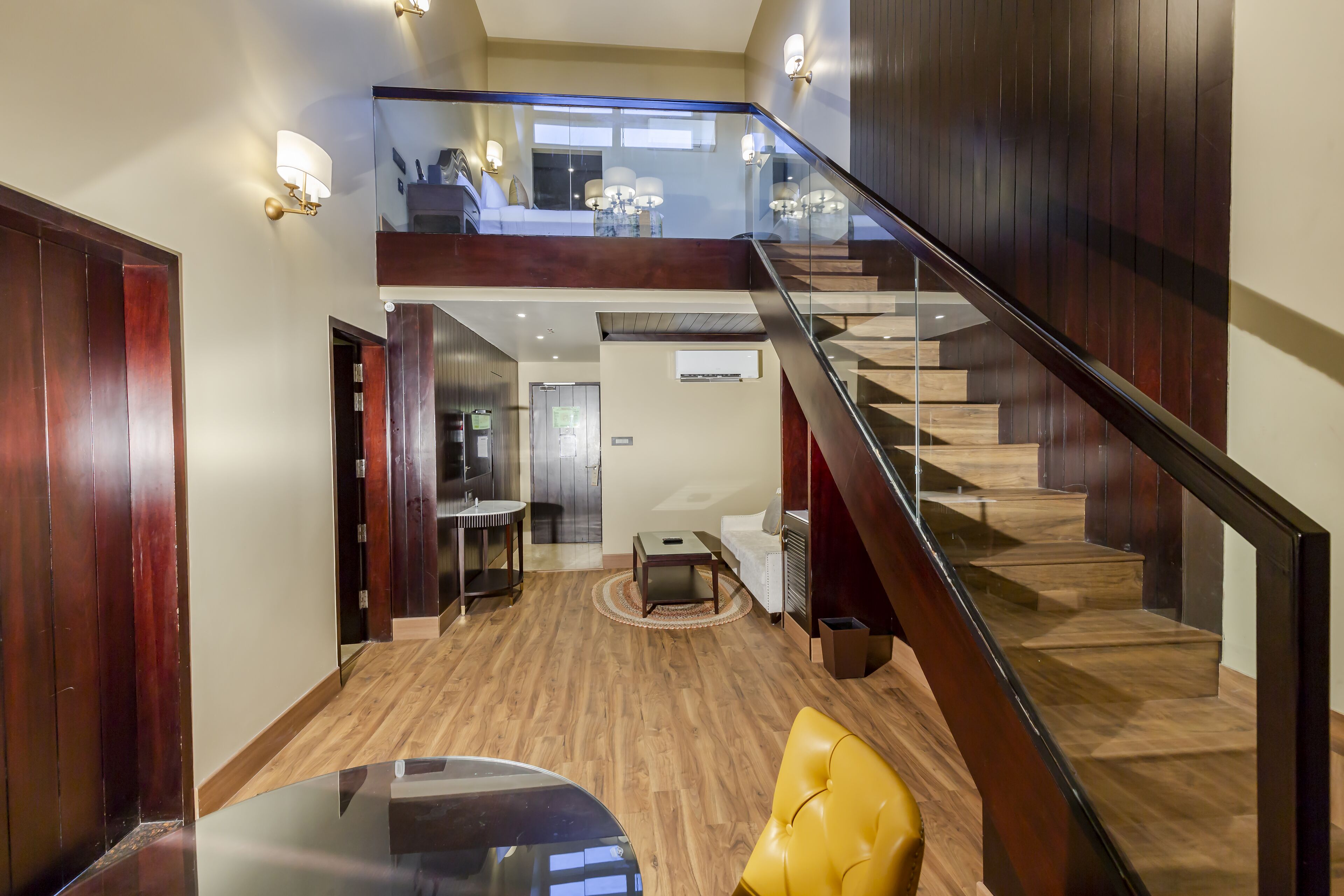 A spacious living area with a wooden staircase, a glass railing, and a dining table.
