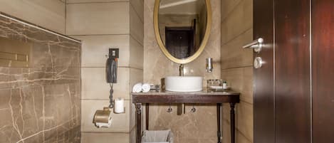 Un baño con pared de mármol, tocador de madera, un espejo grande, inodoro y toallero.