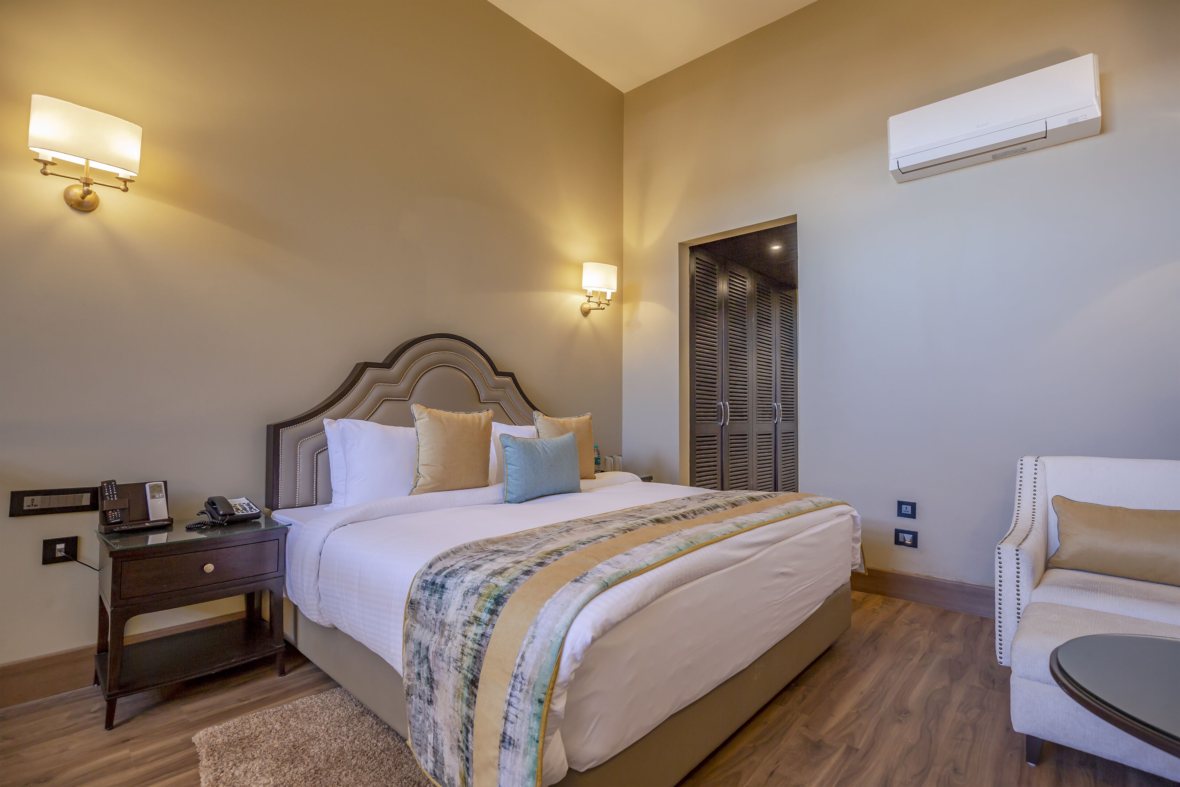A neatly arranged hotel room with a large bed, bedside tables, a chair, and a wardrobe.