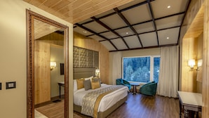 Un dormitorio con una cama grande, una sala de estar con una mesa y sillas, y vistas al exterior a través de una ventana.