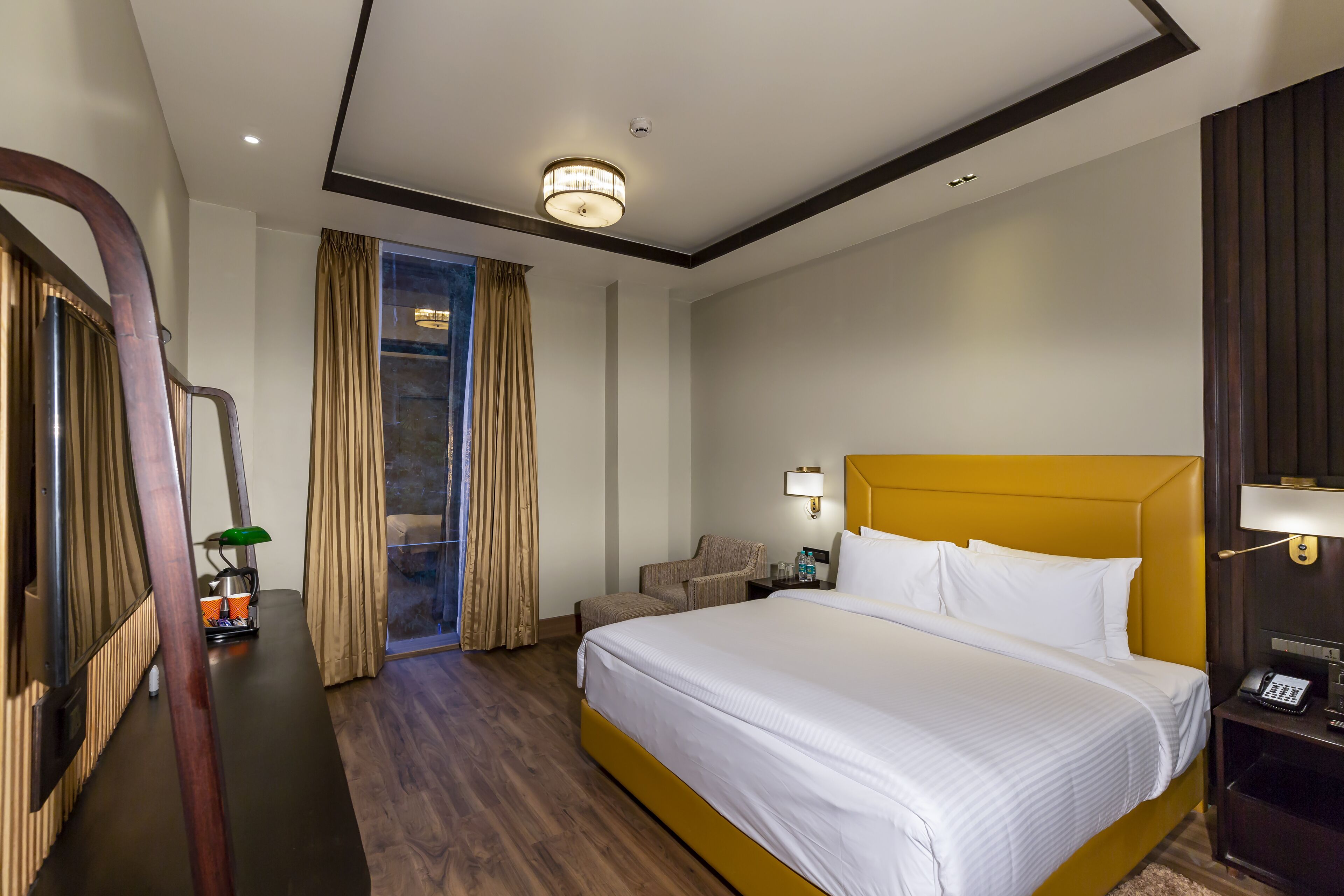 Habitación de hotel con una cama grande, un escritorio con lámpara, una silla y vistas al exterior a través de un ventanal.