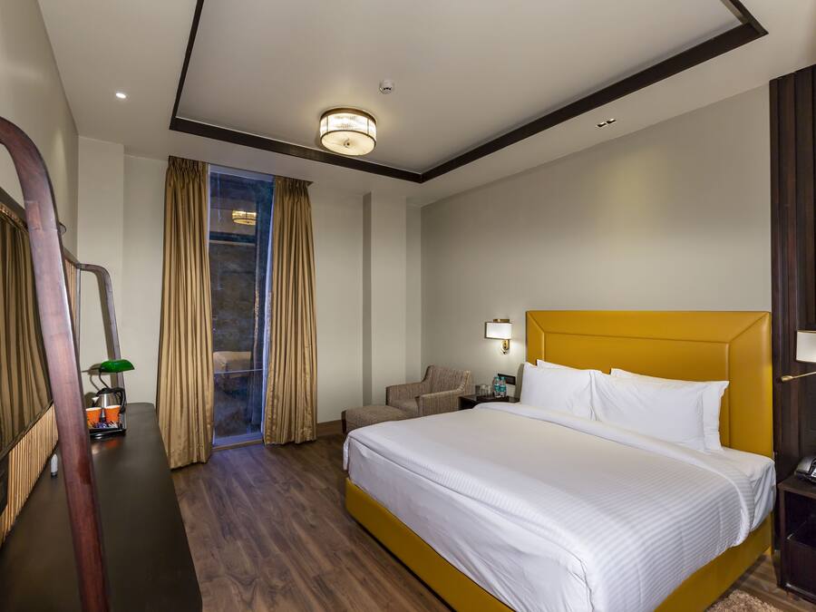 A hotel room with a large bed, a desk with a lamp, a chair, and a view of the outdoors through a glass door.