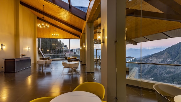 Un interior moderno con techo de madera, ventanas amplias que ofrecen vistas a la montaña y un área de estar con sillas amarillas.