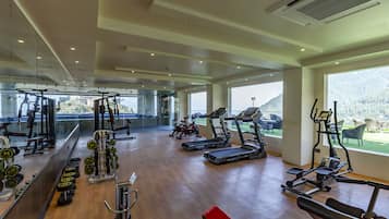 A spacious gym with various exercise equipment, large windows, and a view of mountains.