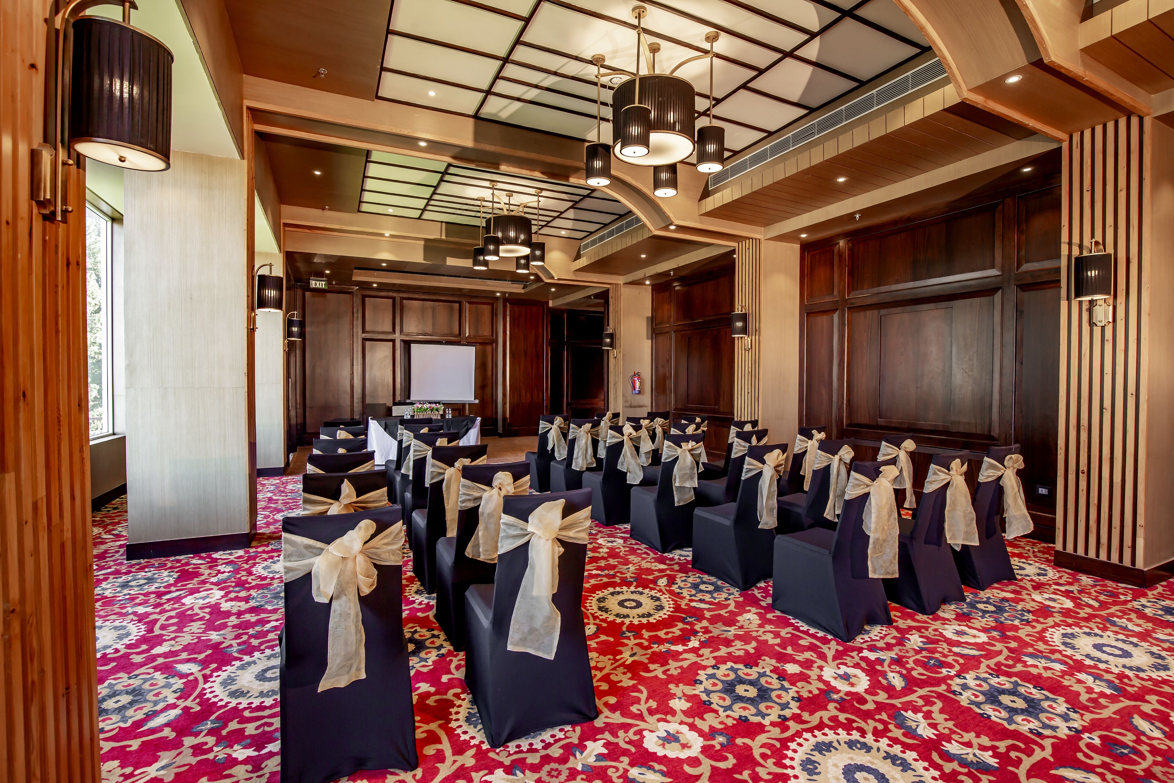 A conference room with rows of chairs, a large screen, and a patterned carpet.