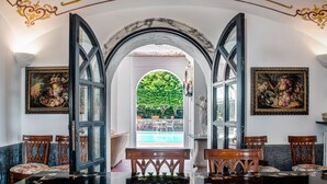 A dining area with a marble archway, wooden chairs, a black table, and a view of a swimming pool. - Palazzo Villa dei Nobili (Sant'Agnello)