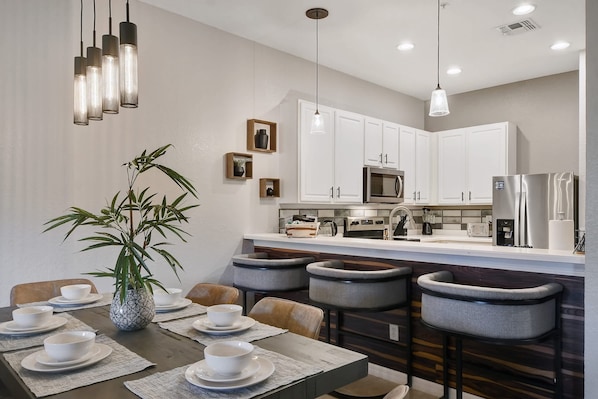 A modern kitchen with white cabinets, a stainless steel refrigerator, and a dining area with a table set for four.