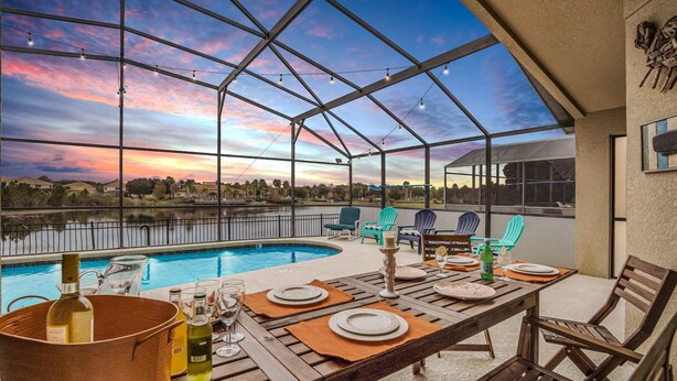 Un espacio exterior cubierto para comer con vista a la piscina, mesas y sillas de madera.