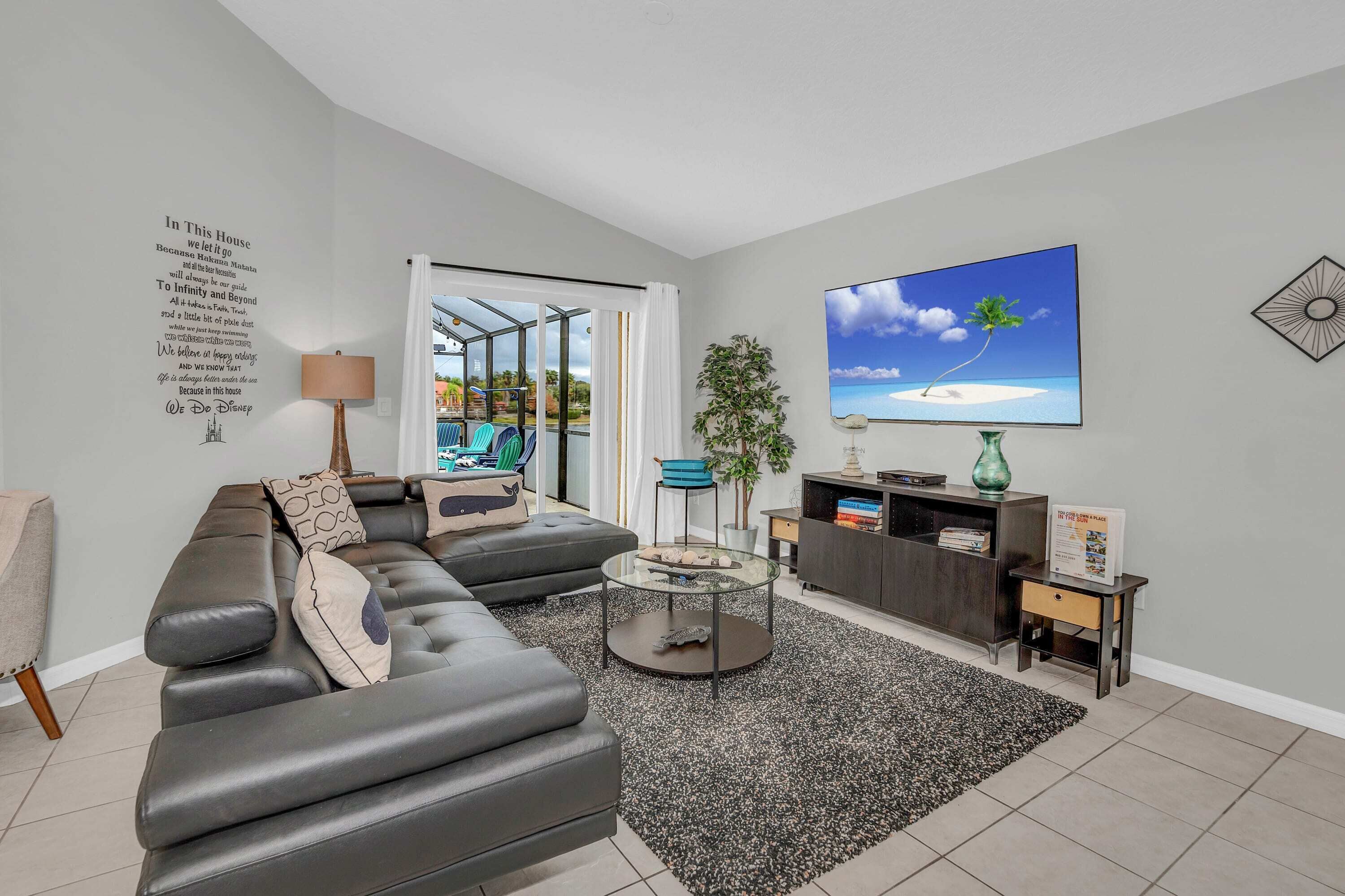 A modern living room with a sectional sofa, a glass coffee table, a TV on the wall, and a view of a pool through a glass door.