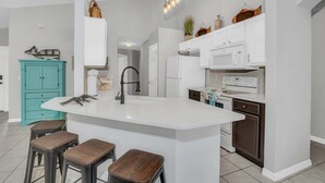Una cocina moderna con armarios blancos, una isla central, taburetes de bar y una lámpara colgante.
