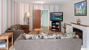 A living room with a sofa, armchair, coffee table, TV, bookshelf, and fireplace. - Te Rangimarie a fully fenced pet friendly home 20minutes walk from the beach. (Himatangi Beach)