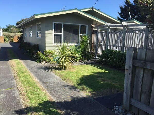 A single-story house with a green roof, a front yard with a small palm tree, and a wooden fence.