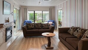 A spacious living room with a large sofa, a smaller sofa, and a coffee table. There is a fireplace on the left and a balcony visible through the windows. - Te Rangimarie a fully fenced pet friendly home 20minutes walk from the beach. (Himatangi Beach)