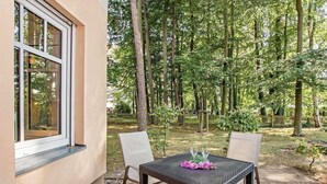 Een terras buiten, met een tafel en stoelen, omringd door bebossing.
