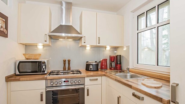 Een moderne keuken met witte kasten, een roestvrijstalen afzuigkap, een magnetron, een gasfornuis en een koffiezetapparaat.
