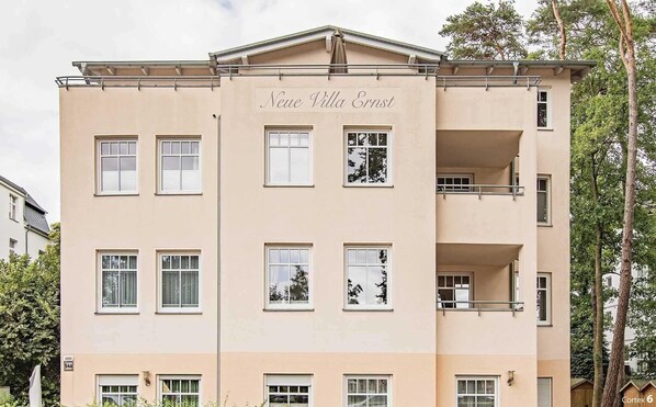 Un immeuble à plusieurs étages, appelé « Neue Villa Ernst », doté d’une façade symétrique, de nombreuses fenêtres et de balcons.